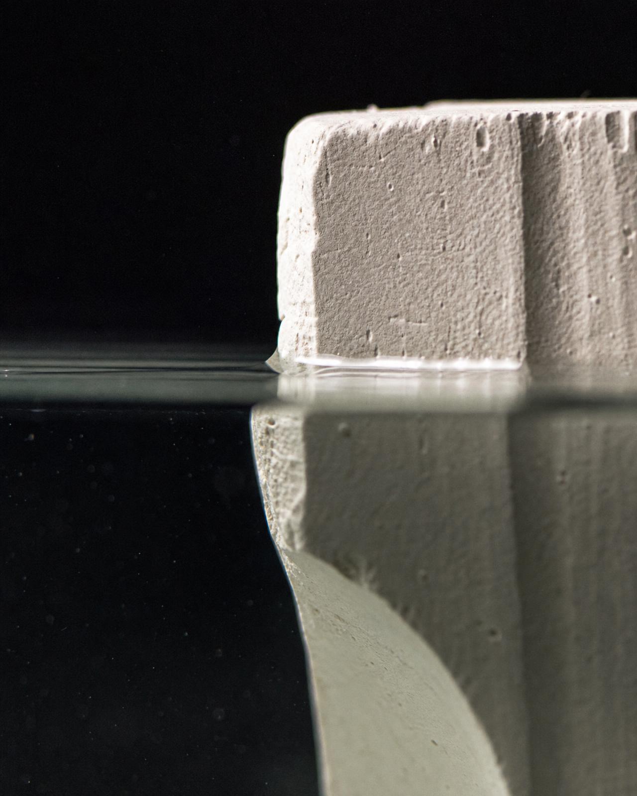 Macro of the waterline where the pale block enters clear water, the submerged half displaced by refraction