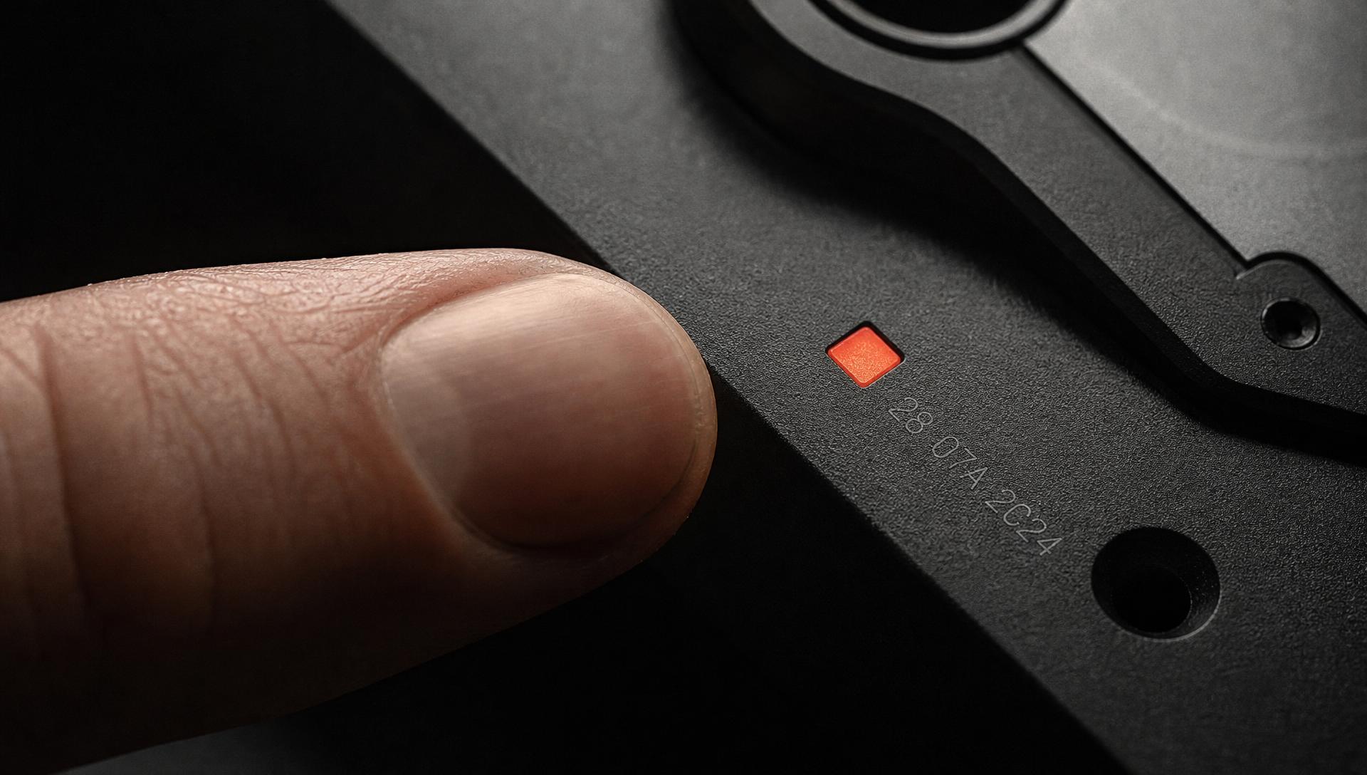 A fingertip approaching the etched black interface panel beside a glowing oxide-red square