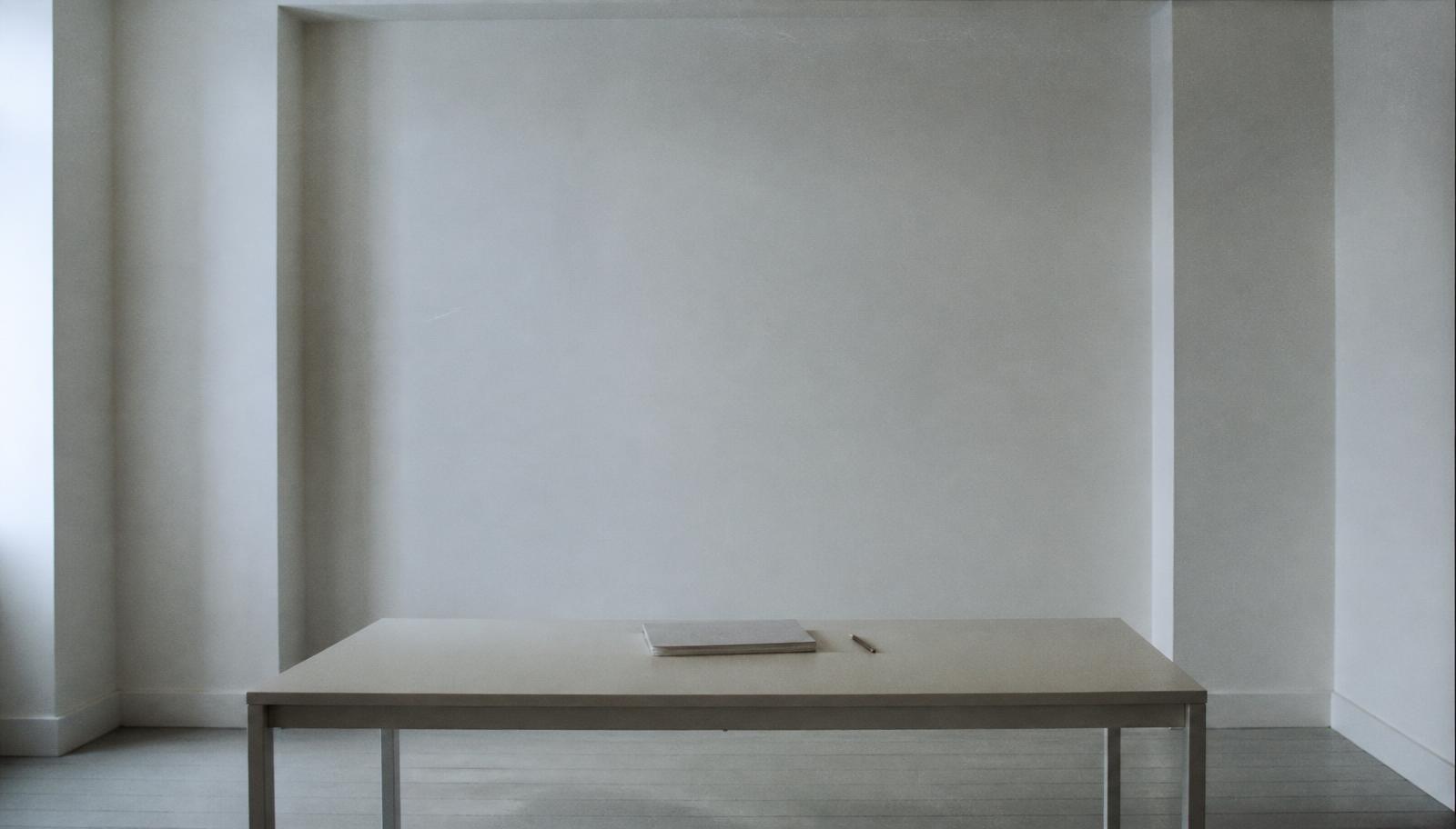 Discarded frame: the same empty white room with a closed sketchbook and no person